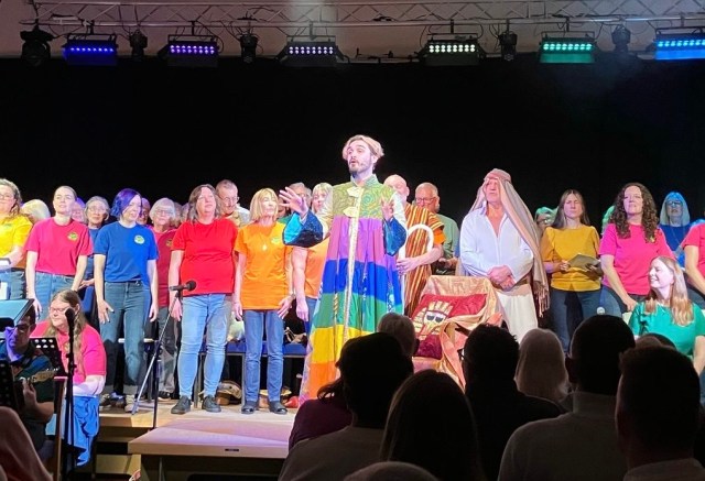 Man dressed as Joseph sings with choir behind him