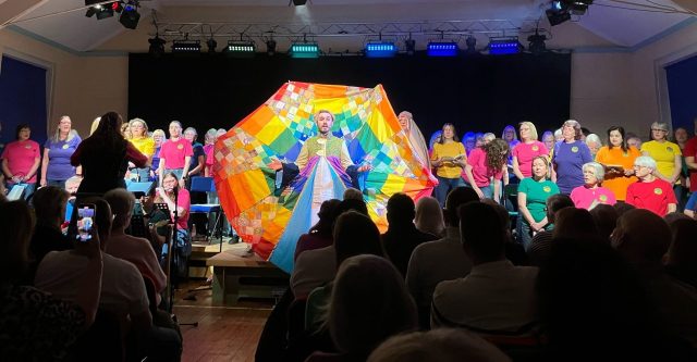 Man in multicoloured coat spread out behind him, singing