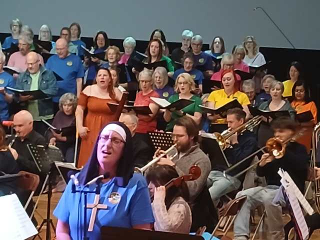 Singer dressed as Mother Superior singing 'Climb Every Mountain' with orchestra in background